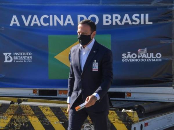 El gobernador de Sao Paulo, Joao Doria, sostiene una dosis de la vacuna CoronaVac contra COVID-19 mientras camina cerca de un contenedor descargado de un avión de carga que llegó desde China al Aeropuerto Internacional de Guarulhos en Guarulhos, estado de Sao Paulo, Brasil, el 18 de diciembre de 2020. - Brasil recibió el viernes el tercer lote con 1.900.000 dosis de la vacuna CoronaVac, desarrollada por el laboratorio chino Sinovac Biotech. (Foto de NELSON ALMEIDA / AFP)