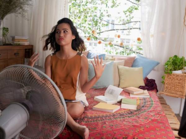 Sweating Asian girl cooling herself with big fan