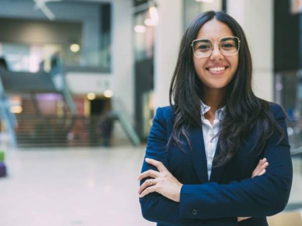 Happy successful businesswoman posing in office hall. Young Latin woman wearing formal suit and glasses, standing for camera with arms folded, smiling. Business portrait concept