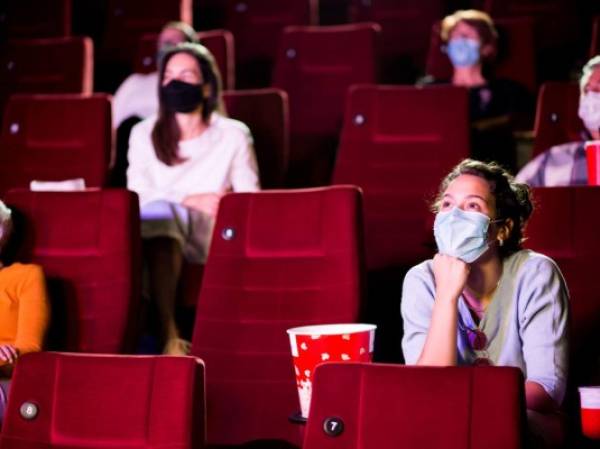 Audience at the cinema wearing protective face masks and sitting on a distance while watching the movie.