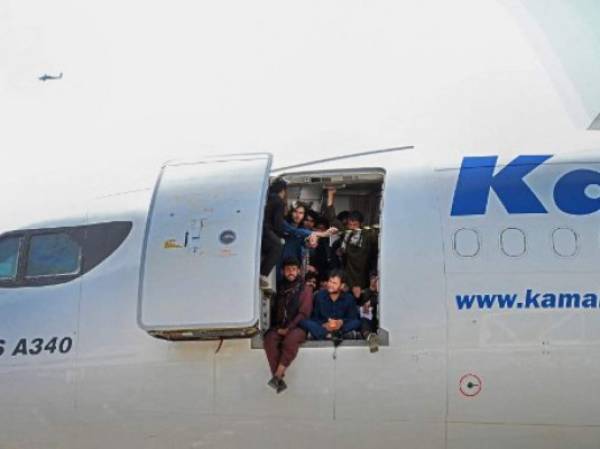 Afghan people climb up on a plane and sit by the door as they wait at the Kabul airport in Kabul on August 16, 2021, after a stunningly swift end to Afghanistan's 20-year war, as thousands of people mobbed the city's airport trying to flee the group's feared hardline brand of Islamist rule. (Photo by Wakil Kohsar / AFP)
