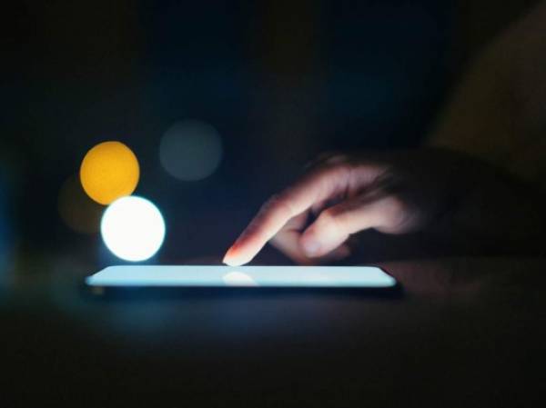 Extremely close-up shot of female finger scrolling on smartphone screen in a dark environment, with bokeh light in the background.