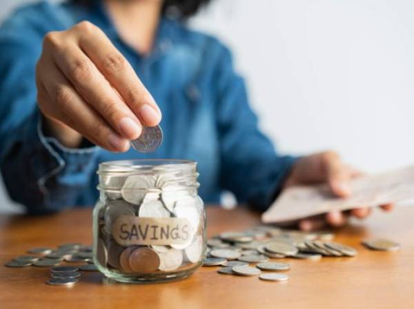 The woman hand is putting a coin in a glass bottle and a pile of coins on a brown wooden table,Investment business, retirement, finance and saving money for future concept.