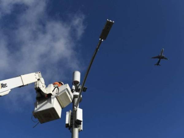 A contractor installs 5G cellular equipment on a light pole as an Alaska Airlines airplane lands at Los Angeles International Airport (LAX) in Inglewood, California on January 19, 2022. - Telecom giants AT&T and Verizon began 5G cell phone data service in the United States Wednesday without major disruptions to flights after the launch of the new wireless technology was scaled back. (Photo by Patrick T. FALLON / AFP)