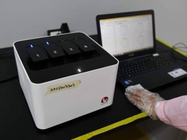 This photo taken on September 27, 2020 shows a technician in Beijing checking test results using the Flash 20 (L), a machine developed by Chinese biotech company Coyote as a fast test for the COVID-19 coronavirus. (Photo by GREG BAKER / AFP)