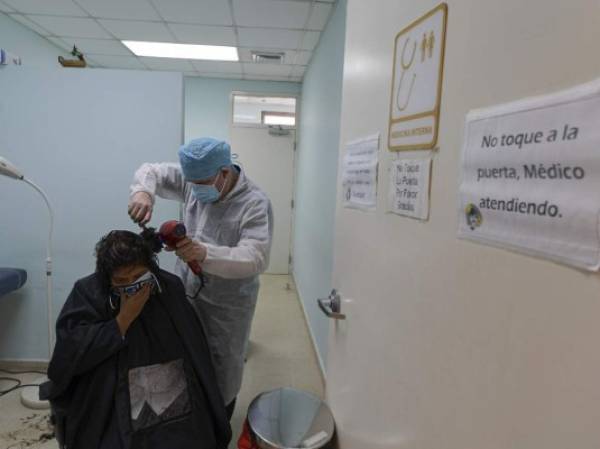 A nurse has her hair done at the consulting room of the Hospital Santo Tomas in Panama City on August 14, 2020 amid the COVID-19 novel coronavirus pandemic. - While hair salons have been closed for months and are expected to reopen next week, doctors and nurses at the Santo Tomas Hospital received free haircuts as an incentive for their work in the fight against COVID-19. (Photo by Luis ACOSTA / AFP)