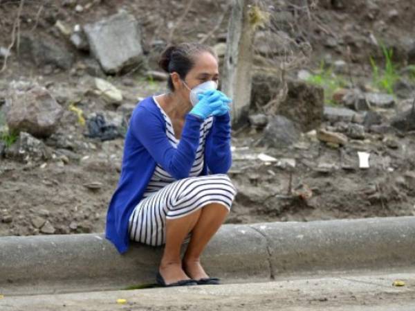 A woman wearing a face mask and gloves uses waits next waits outside a cemetery in Guayaquil, Ecuador on April 1, 2020. - Residents of Guayaquil, in Ecuador's southwest, express outrage over the way the government has responded to the numerous deaths related to the novel coronavirus, COVID-19, saying there are many more deaths than are being reported and that bodies are being left in homes for days without being picked up. Ecuador marked its highest daily increase in deaths and new cases of coronavirus on Sunday, with the total reaching 14 dead and 789 infected, authorities had said. (Photo by Marcos Pin / AFP)