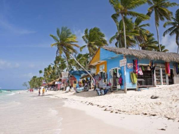 Punta Cana, Dominican Republic- July 20, 2013: Tourist walking on the beach and take a tour of the bungalows-stalls with souvenirs. Locals sitting in front of stalls