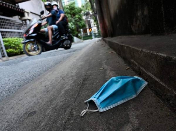 Motorist wearing facemasks amid fears over the spread of the COVID-19 novel coronavirus ride past a facemask left on an alley in Bangkok on March 26, 2020. - A state of emergency came into force in Thailand on March 26 aimed at halting the spread of the virus. (Photo by Romeo GACAD / AFP)