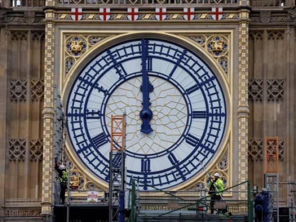Workers remove the scaffolding from the restored west dial of the clock on Elizabeth Tower, commonly known by the name of the bell Big Ben, at the Palace of Westminster, home to the Houses of Parliament, in London on December 20, 2021. - The dial of the famous clock was revealed after undergoing repairs as part of the Elizabeth Tower conservation project that has seen the whole tower covered in scaffolding and silenced for months. (Photo by Tolga Akmen / AFP)