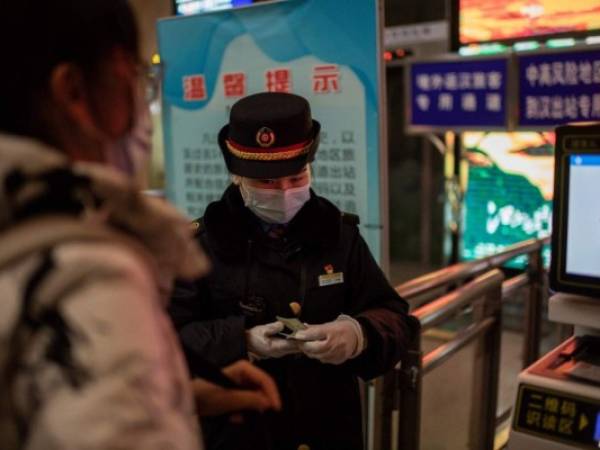 Un controlador ferroviario verifica la identificación de un viajero a su llegada a la estación principal de trenes de Wuhan el 10 de enero de 2021, la víspera del primer aniversario de China que confirma su primera muerte por el coronavirus Covid-19. (Foto de NICOLAS ASFOURI / AFP)