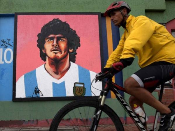 A man on bicycle passes by a mural depicting late Argentine football star Diego Maradona, in Bogota on November 23, 2021. - November 25 marks the first anniversary of Diego Maradona's death. he died from a heart attack at the age of 60. (Photo by Raul ARBOLEDA / AFP)