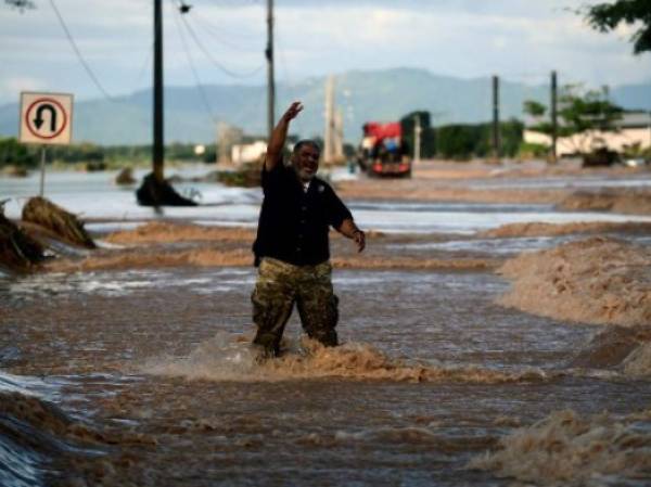 Two locals chat while standing nearby the flooded road to San Pedro Sula, following the passage of Hurricane Eta, near the locality of Campin, 240km north of Tegucigalpa, on November 7, 2020. - Scores of people have died or remain unaccounted for as the remnants of Hurricane Eta unleashed floods and triggered landslides on its deadly march across Central America. (Photo by Orlando SIERRA / AFP)