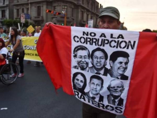 Un peruano sostiene una bandera del Perú con los rostros de Alberto Fujimori, Alejandro Toledo, Ollanta Humala, Alan Garcia, además de la exprimera dama Nadine Heredia sobre quienes pesan señalamientos de corrupción.