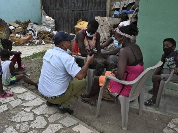 Un policía municipal habla con migrantes haitianos mientras esperan que la oficina de migraciones les dé un resguardo para continuar su camino en una caravana rumbo a Estados Unidos, en el municipio de Trojes, departamento de El Paraíso, Honduras, en la frontera con Nicaragua, el 21 de abril. , 2021. - La vicealcaldesa de Trojes, Dinora Sandoval, dijo a la AFP que un promedio de 400 personas provenientes de países africanos como Costa de Marfil, Ghana y Senegal, haitianos, cubanos y otros ingresan diariamente al municipio. (Foto de Orlando SIERRA / AFP)