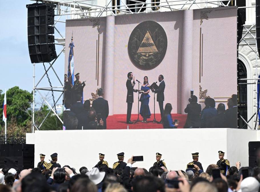 <i>La gente observa en una pantalla gigante mientras el presidente de El Salvador, Nayib Bukele (i), jura junto a su esposa Gabriela Rodríguez (centro) y al presidente del Congreso, Ernesto Castro, en el Palacio Nacional, en el centro de San Salvador, el 1 de junio de 2024. (Foto de Marvin Recinos / AFP)</i>